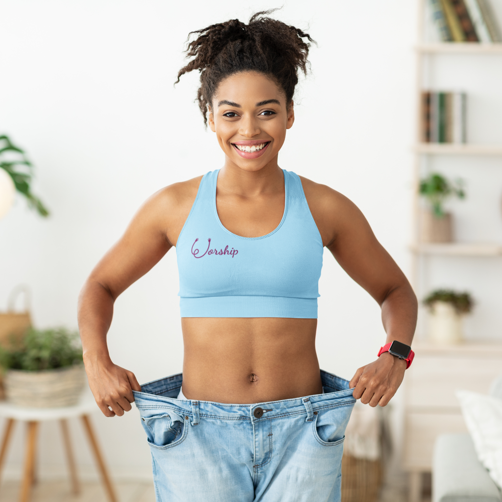 Joyful fit woman wearing a blue Worship Sports Bra by Fitness for Worship and standing in pants that are too large