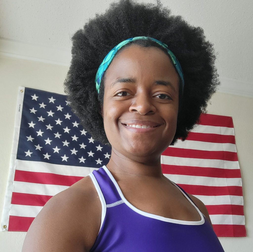 Michelle Barnes standing in front of American flag wearing Royalty Sports Bra & Green Gems Headband by Fitness for Worship
